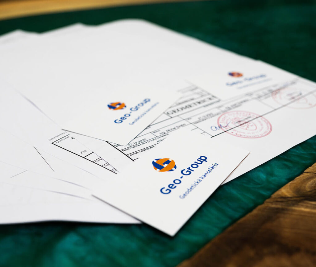 Geometrické plány geodetickej kancelárie Geo-Group rozložené na stole, na jednom z nich je okrúhla pečiatka autorizačného overenia a podpis geodeta. Ilustruje autorizačné overenie geometrického plánu.